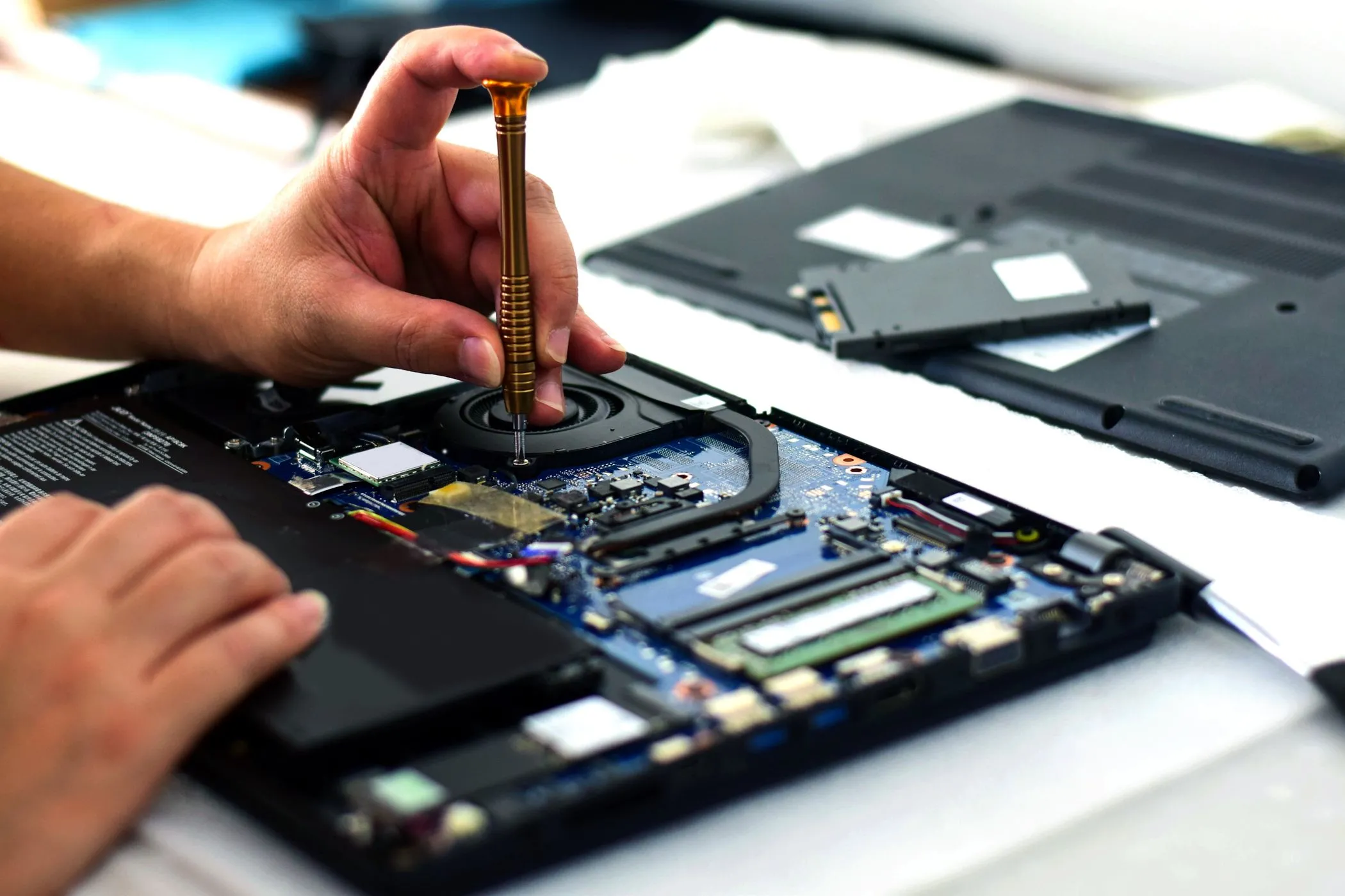 Kỹ thuật viên đang sửa chữa bo mạch chủ laptop bằng tuốc nơ vít, phản ánh thách thức trong việc sửa chữa các mẫu laptop mỏng nhẹ.