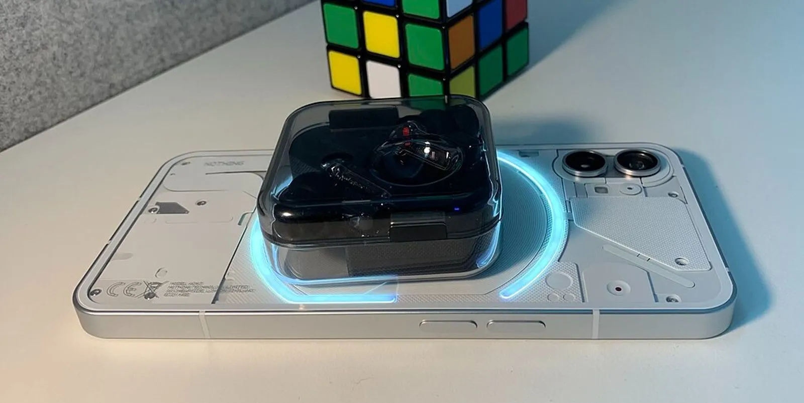 Điện thoại Nothing Phone (1) đang sạc không dây ngược cho tai nghe true wireless, đặt cạnh khối Rubik.