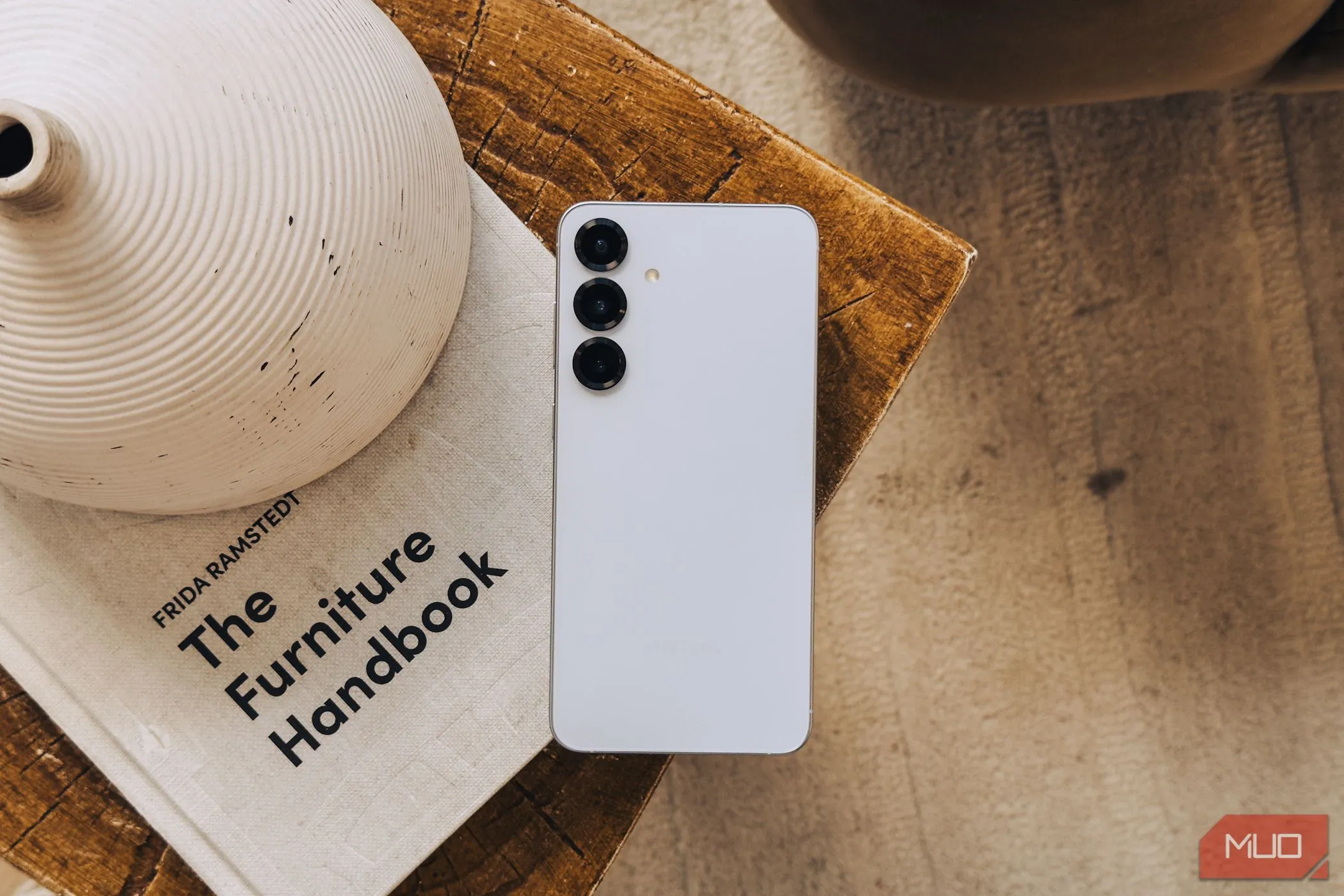 Điện thoại Samsung Galaxy S25 màu bạc đặt trên cuốn sách trắng, thể hiện thiết kế và cụm camera sau của thiết bị.
