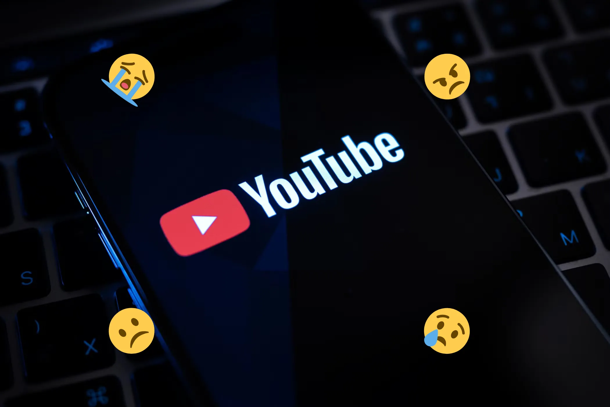 Một chiếc điện thoại thông minh hiển thị logo YouTube trên màn hình, bao quanh bởi các biểu tượng cảm xúc buồn và tức giận