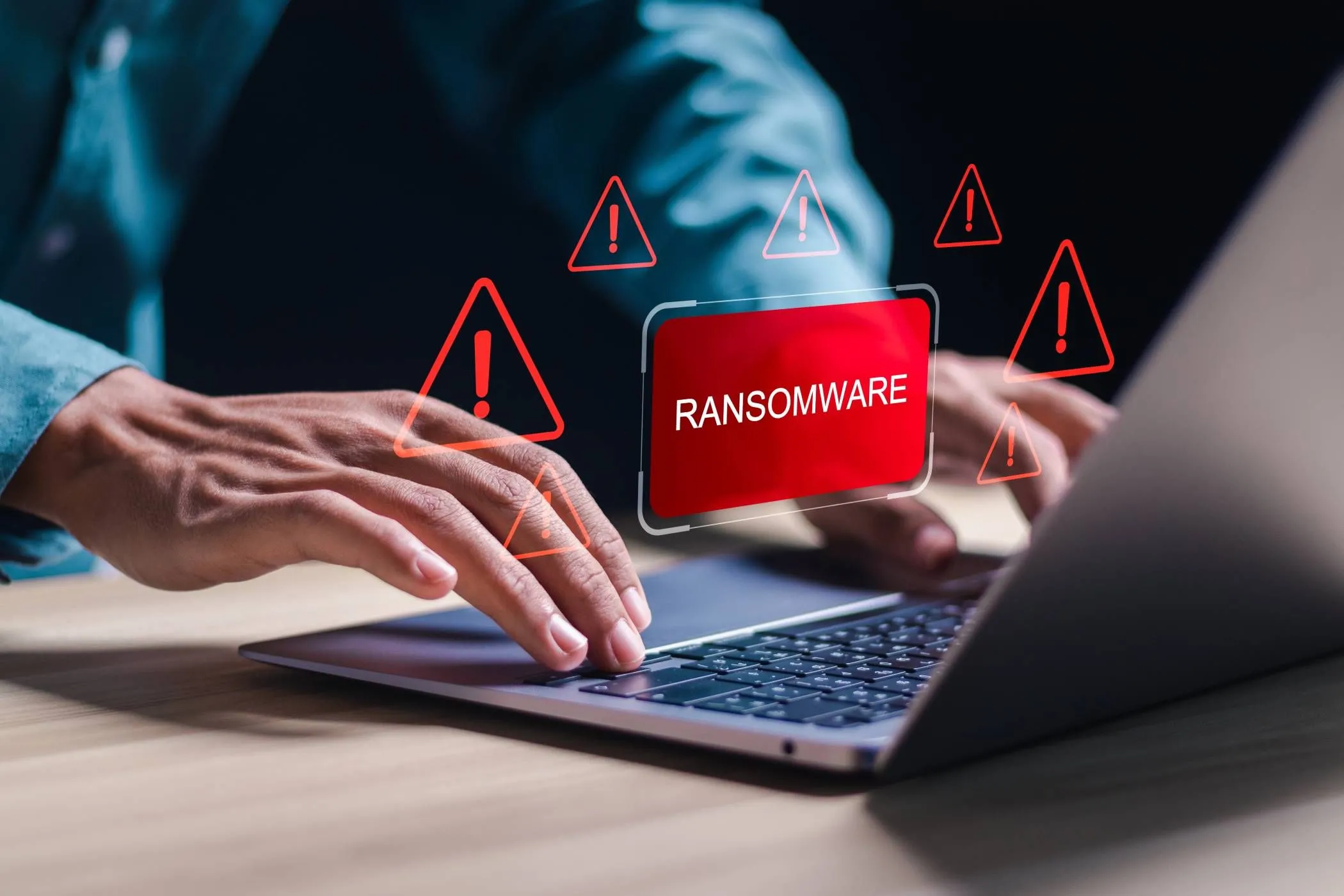 Người dùng đang làm việc trên laptop với biểu tượng ransomware, thể hiện nguy cơ mã độc tống tiền đối với dữ liệu và hệ thống.