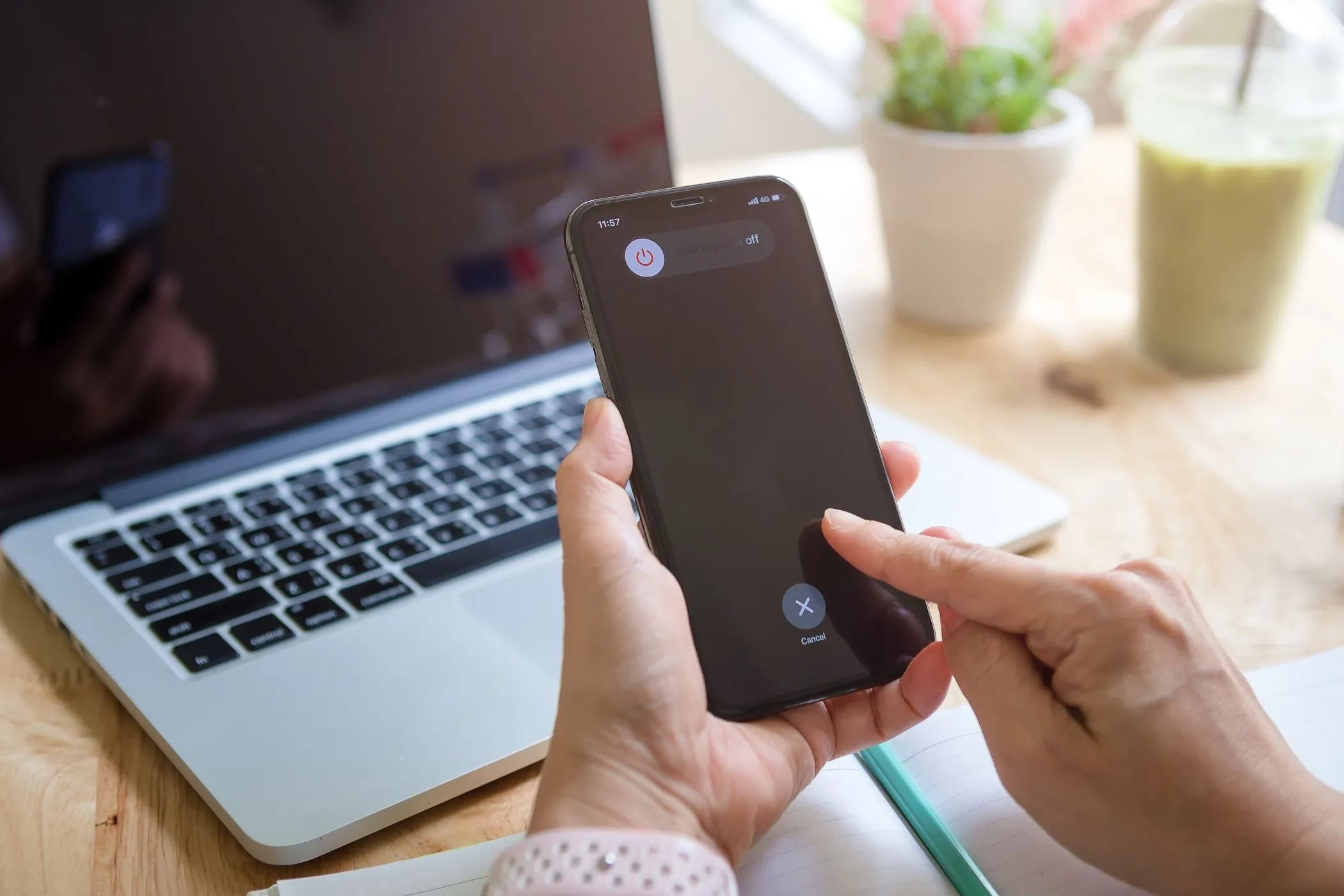 Người phụ nữ đang tắt nguồn iPhone với MacBook ở nền, liên quan đến lầm tưởng sạc nhanh hơn khi tắt máy