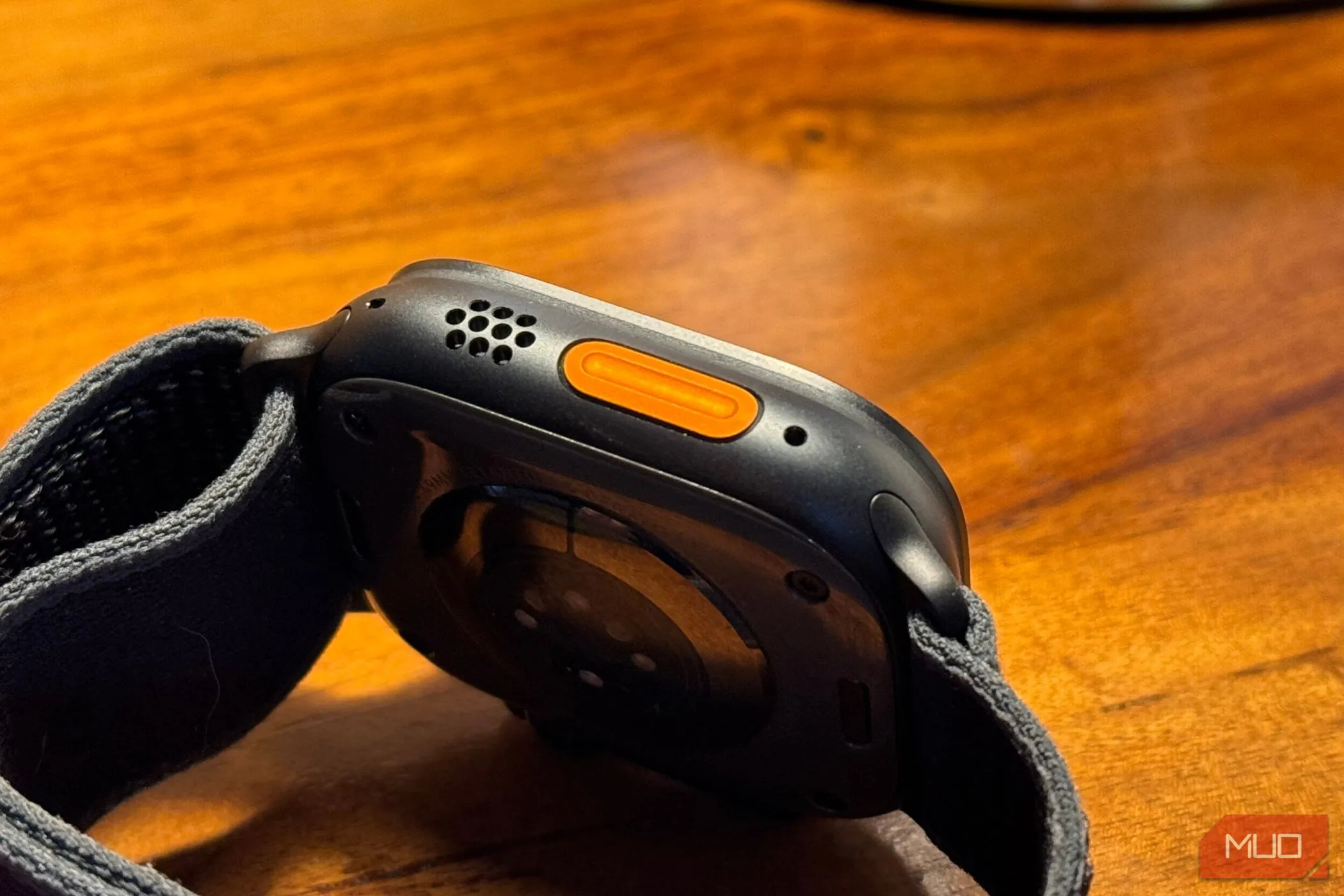 Nút Tác vụ (Action Button) nổi bật trên thân đồng hồ Apple Watch Ultra 2 màu titan đen đặt trên bàn