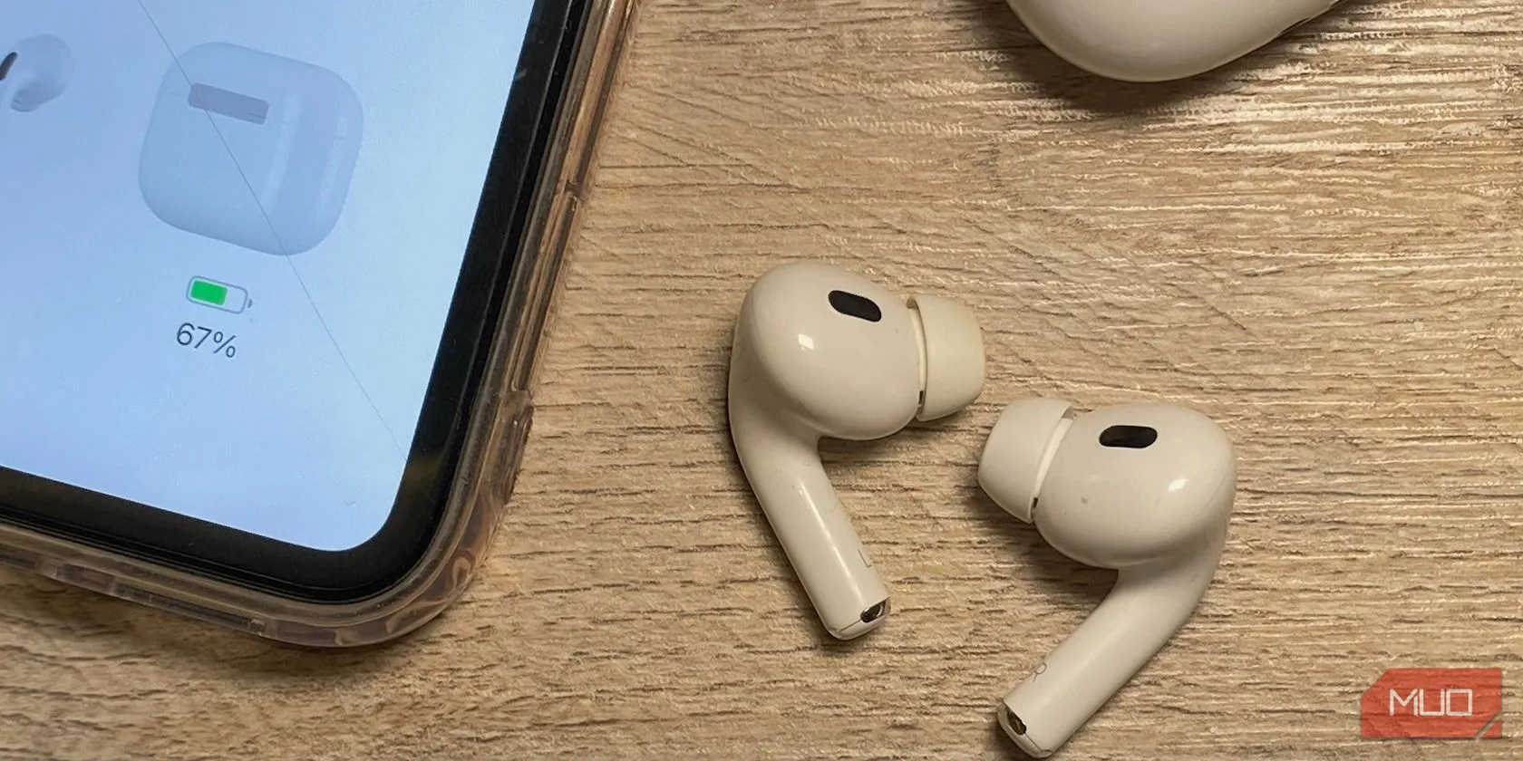 Tai nghe AirPods đời thường đặt cạnh iPhone trên bàn gỗ, minh họa sự khác biệt về chiều dài thân giữa các thế hệ.